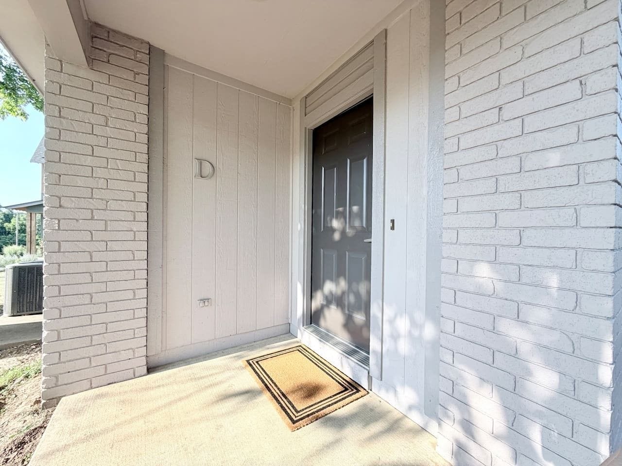 A white brick exterior with a dark door, a doormat, and a small step leading to the entrance.