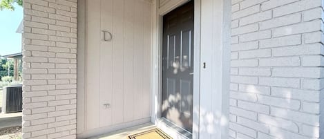 A white brick exterior with a dark door, a doormat, and a small step leading to the entrance.