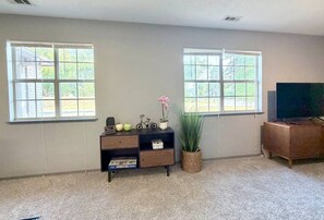 Uma sala de estar com duas janelas, uma televisão, um armário e uma planta.