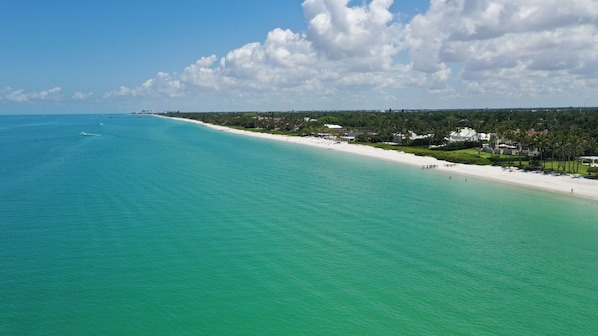 A coastal view with a beach, clear turquoise water, and a line of buildings along the shore. - Beautiful Vacation Home with Saltwater Pool and Spa, Lake View and SW Exposure (Naples)