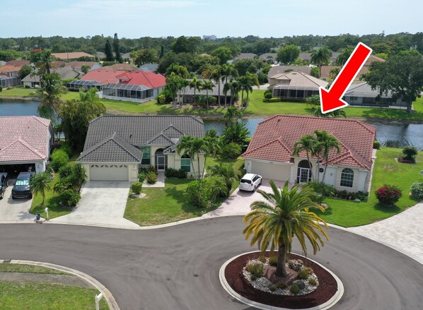 A residential area with houses, a lake, and a red arrow pointing to a house with a red roof. - Beautiful Vacation Home with Saltwater Pool and Spa, Lake View and SW Exposure (Naples)