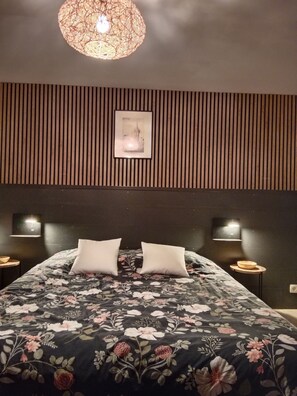 A bedroom with a large bed, two bedside tables, a wall-mounted picture, and a hanging light fixture. - Hapiness Cottage (Colmar)
