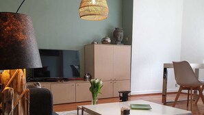En moderne stue med sofa, sofabord og lampe. Der er et fjernsyn, skab og en lænestol.