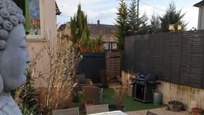 En patio med spiseplads, et bord og stole. En statue i forgrunden og en grill i baggrunden.