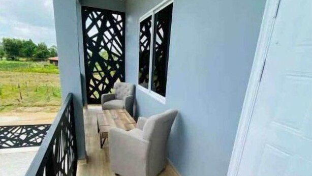 Een balkon met een houten vloer, een grijze bank en een zwart lattenwand.