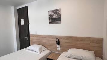 Habitació d'hotel amb dos llits individuals, un capçal de llit de fusta, una petita taula de nit, un telèfon fixat a la paret i una porta amb un paper enganxat.