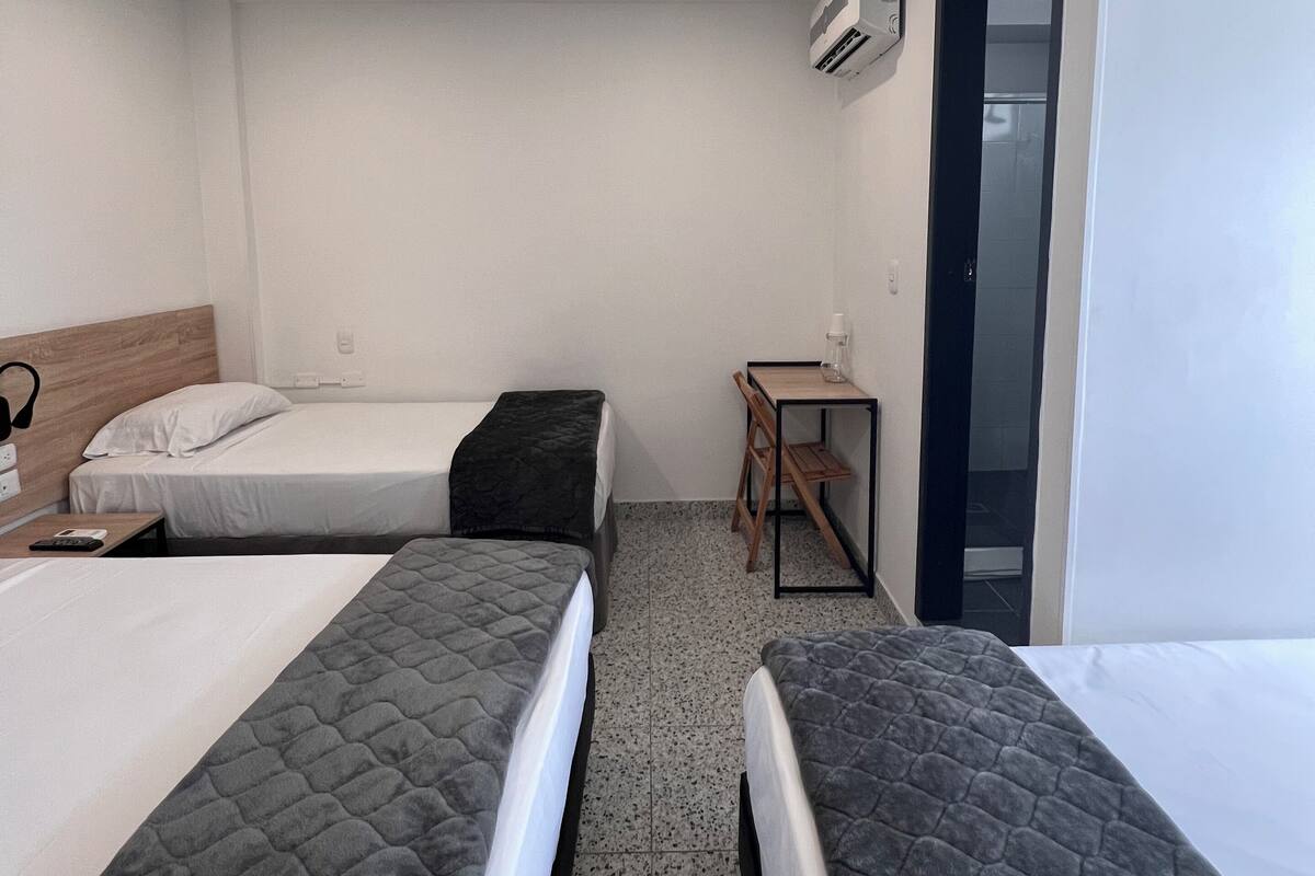 Una habitación de hotel con dos camas, una mesita pequeña y un equipo de aire acondicionado.