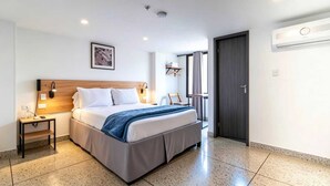 Habitación de hotel moderna con cama, mesita de noche, lámpara y vistas al exterior.