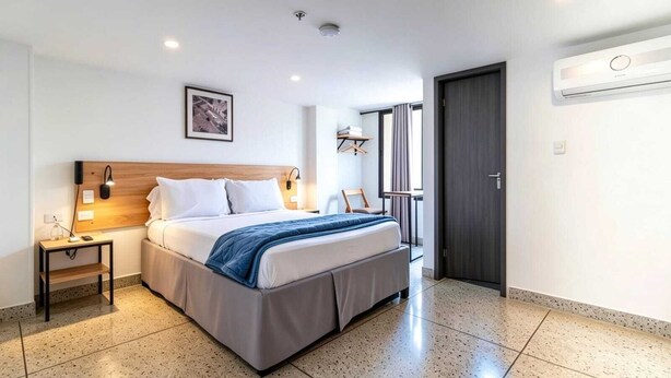 A modern hotel room with a bed, bedside table, lamp, and a view of the outside.