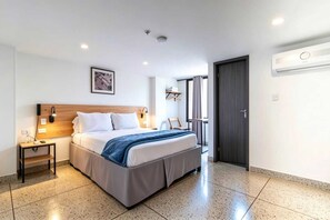 Une chambre d’hôtel moderne, équipée d’un lit, d’une table de chevet, d’une lampe et offrant une vue sur l’extérieur.