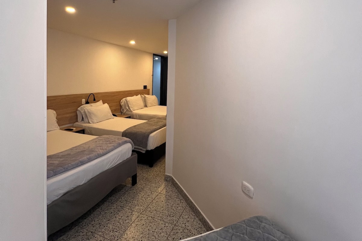 Habitación de hotel con dos camas, un pequeño rincón de descanso y una puerta que da a otra habitación.