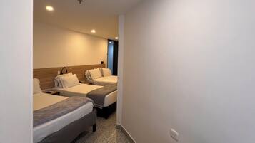 Quarto de hotel com duas camas, um espaço de estar pequeno e uma porta que dá para outro cômodo.