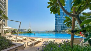 A swimming pool with lounge chairs and a view of a tall building in the background. - Luxury StayCation - Incredible Sea View Apartment With Balcony (Dubai)