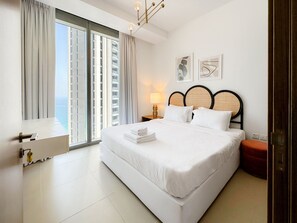 A modern hotel room with a large bed, a nightstand, a lamp, and artwork on the wall. - Luxury StayCation - Incredible Sea View Apartment With Balcony (Dubai)