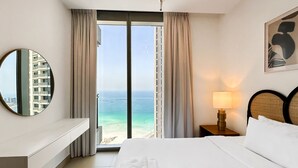 A hotel room with a bed, a nightstand with a lamp, a mirror, and a view of the ocean. - Luxury StayCation - Incredible Sea View Apartment With Balcony (Dubai)