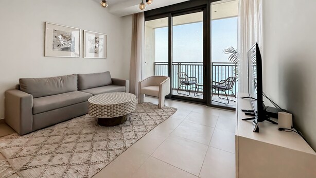 A modern living room with a grey sofa, a patterned ottoman, and a ceiling light fixture. - Luxury StayCation - Incredible Sea View Apartment With Balcony (Dubai)