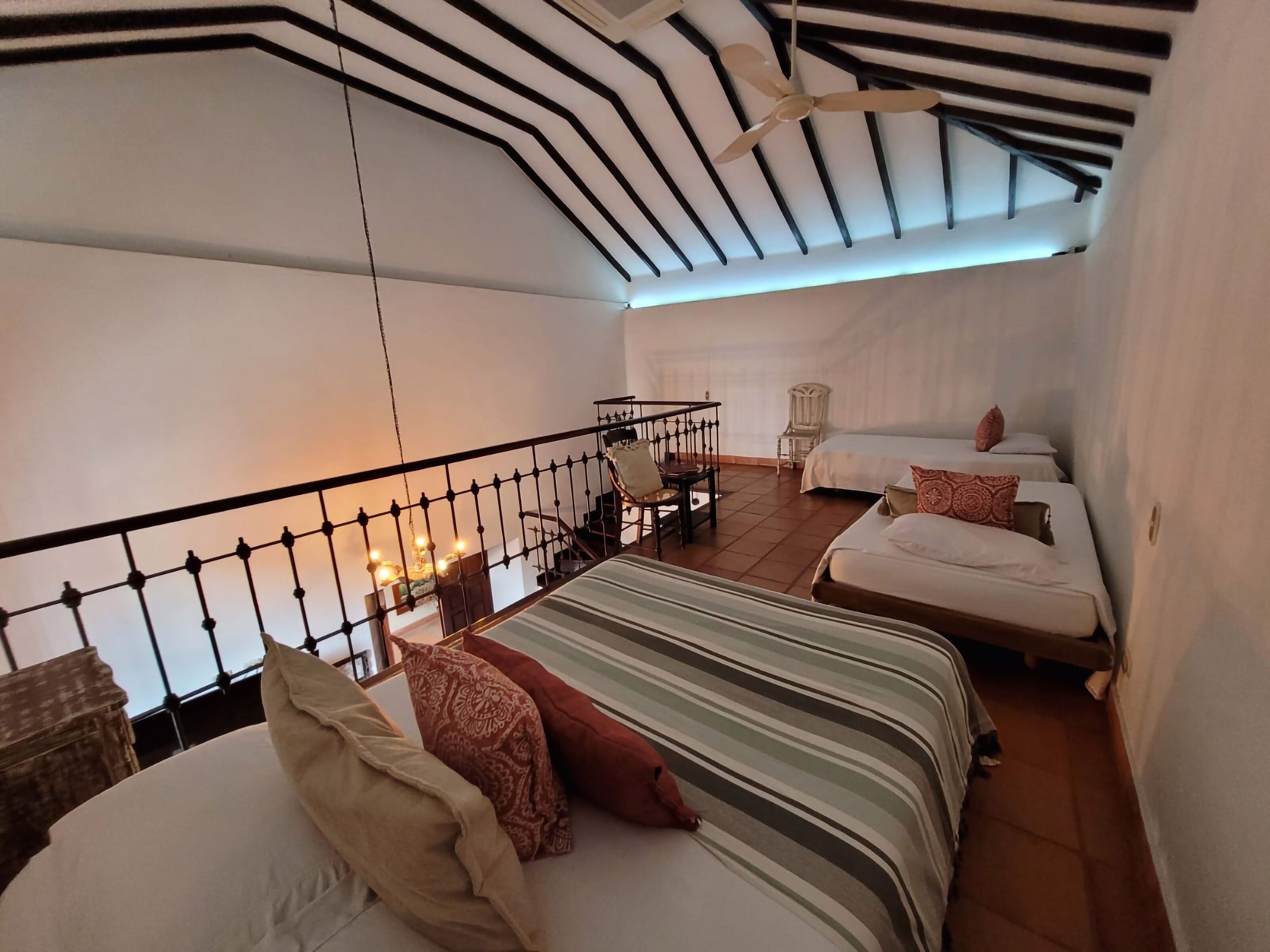 Habitación con dos camas, ventilador de techo y balcón con barandilla.