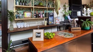Zona de bar con mostrador de madera, un cartel que dice 'Bar' y un bol de manzanas verdes. Hay estantes con botellas y un espejo arriba.