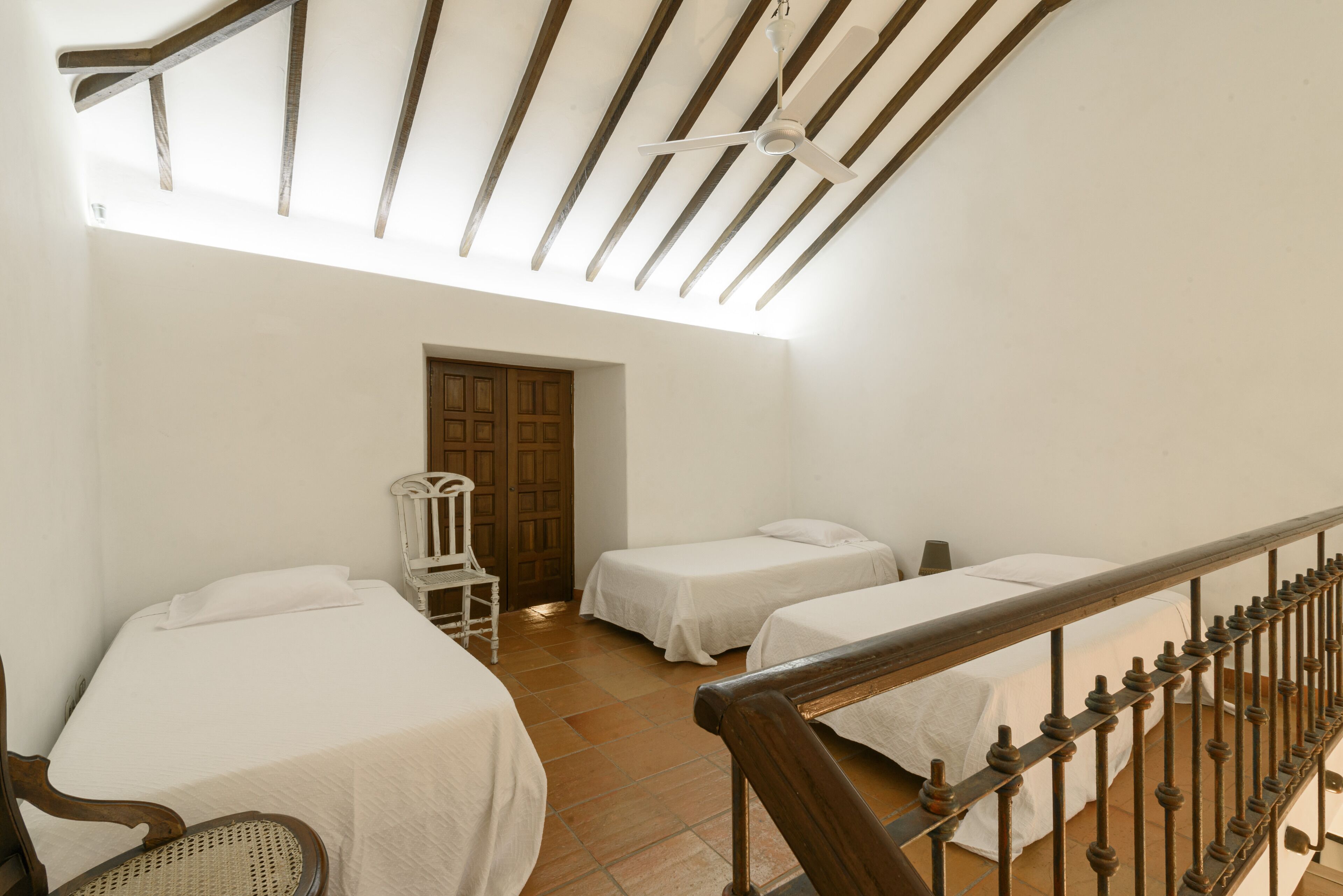 A room with two beds, a wooden chair, and a wooden staircase.