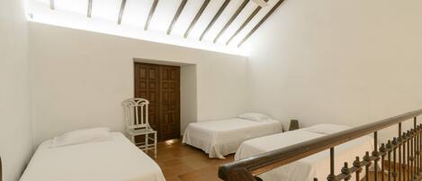 A room with two beds, a wooden chair, and a wooden staircase.
