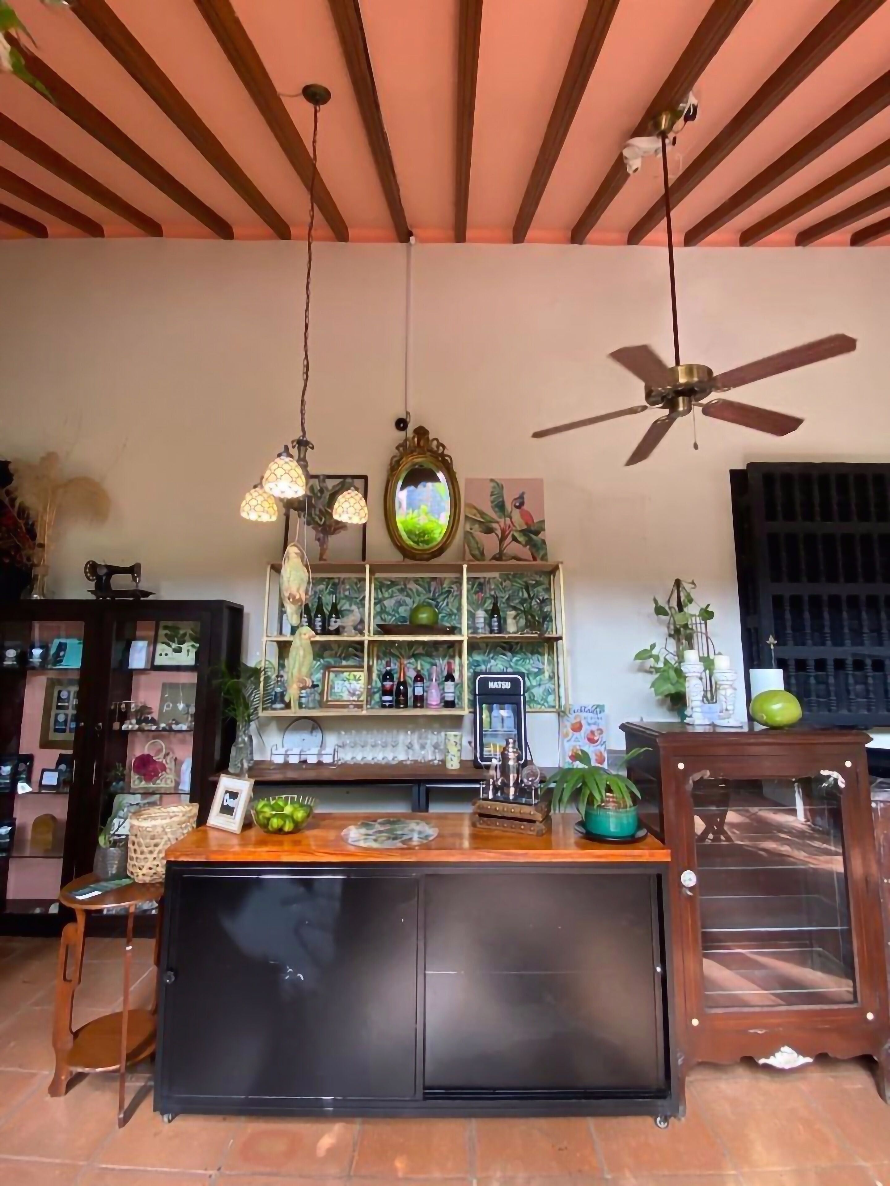 A bar area with a wooden ceiling, hanging lamps, a ceiling fan, and shelves with bottles and decorative items.