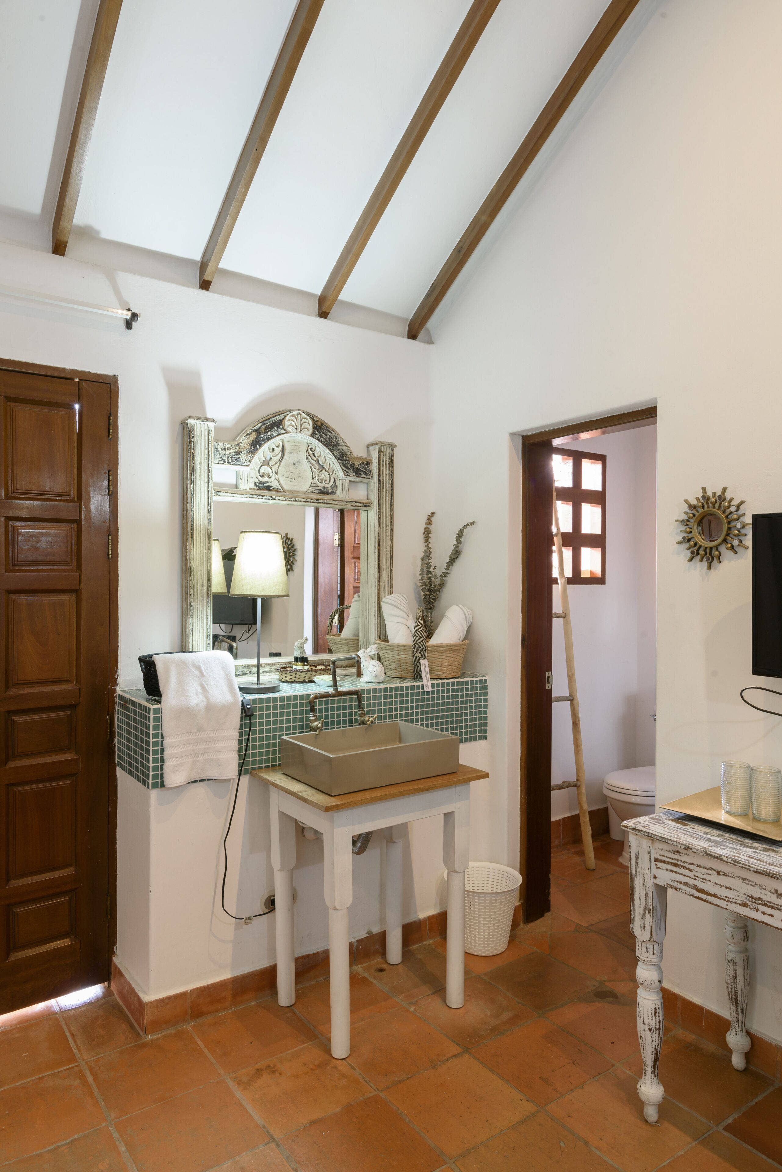 A bathroom with a tiled floor, a sink, a mirror, and a wooden door.