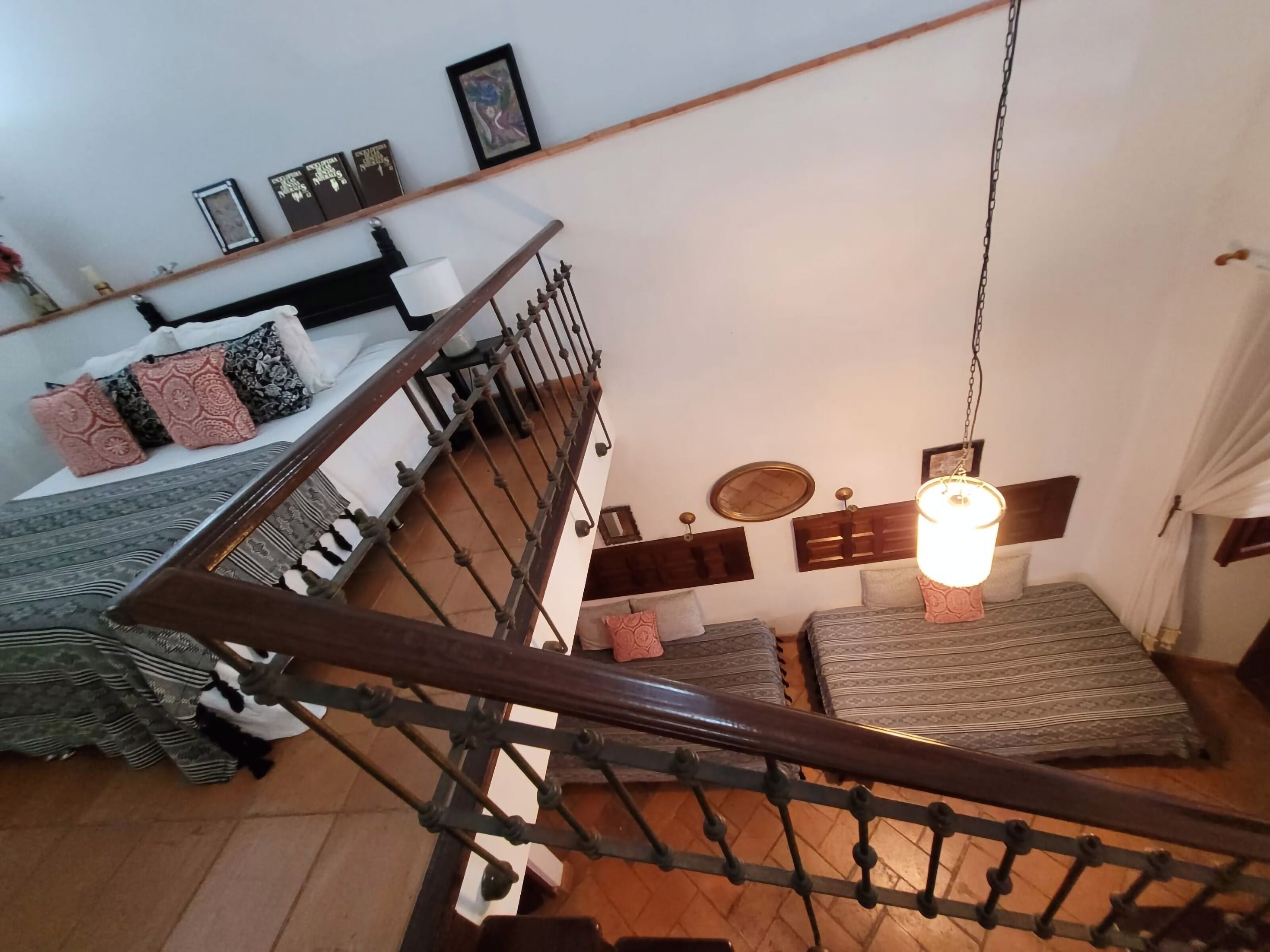 Una escalera que lleva a un dormitorio con cama, almohadas y una lámpara colgante.