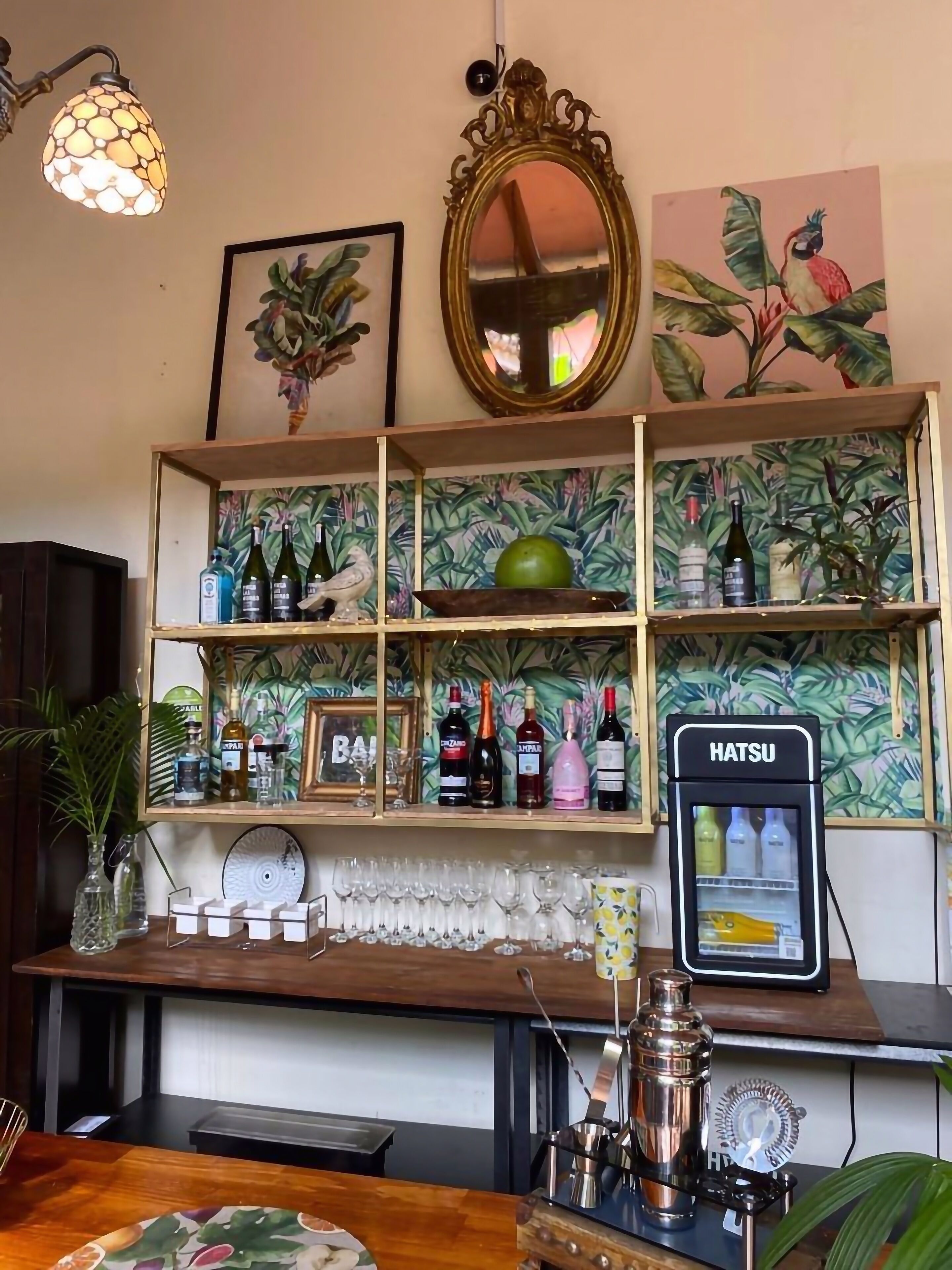 Een bar met drankflessen op de planken, een Hatsu koelkast en een spiegel boven de bar.