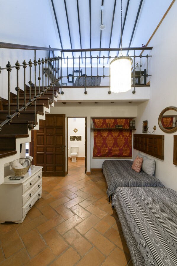 A spacious loft bedroom with a wooden staircase, a large bed, a hanging light fixture, and a view of the sky through the skylight. - Hotel Boutique Al Alma (Santa Fe de Antioquia)