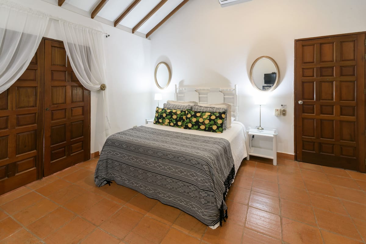 A bedroom with a bed, two bedside tables, a nightstand, a mirror, and two doors.