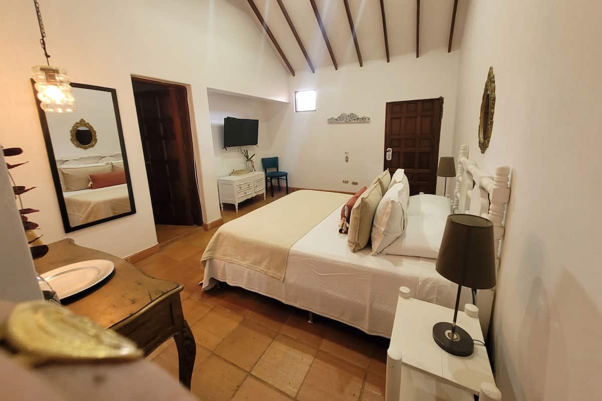 A hotel room with a bed, a desk, a chair, a TV, and a mirror.