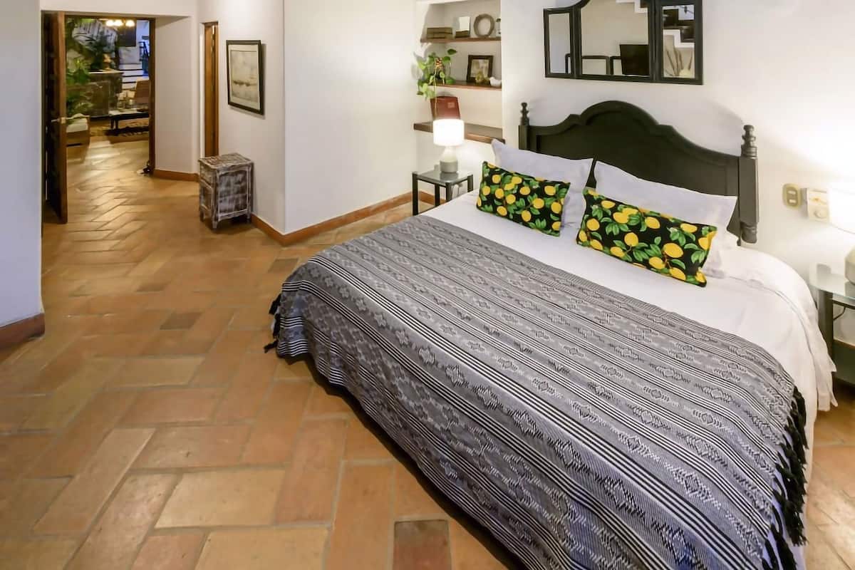 A spacious bedroom with a large bed, a ceiling fan, a chandelier, and a view of the outdoors.