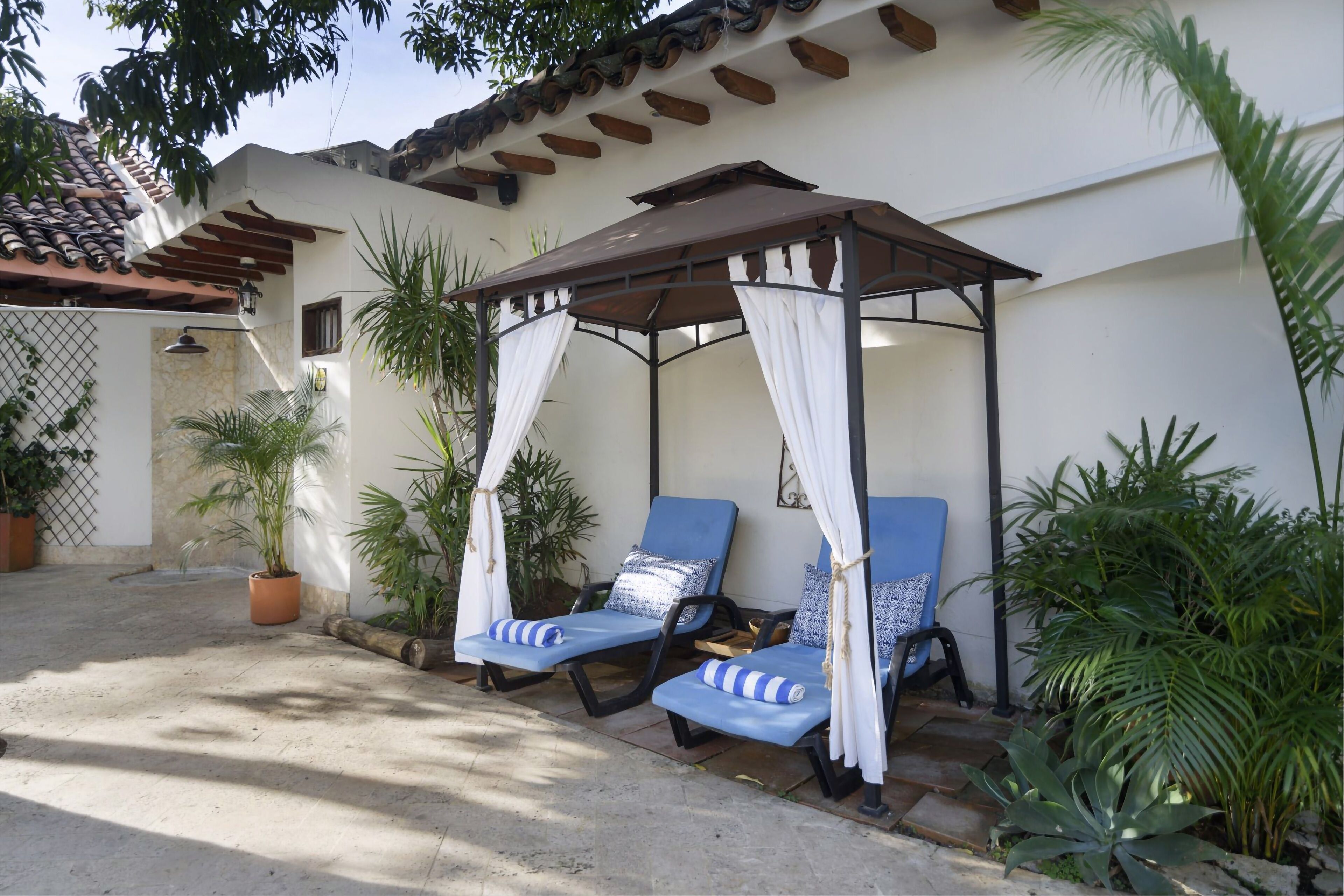 A covered outdoor seating area with two blue lounge chairs and a canopy.