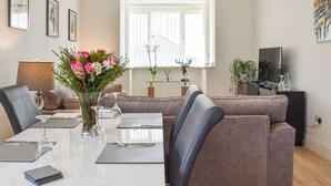 A modern living room with a dining area, featuring a sofa, a coffee table, and a TV. - A beautiful bungalow overlooking the coastal town of Llanelli. (Llanelli)
