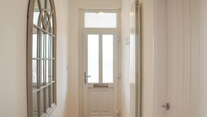 A hallway with a white door, a window with a grid pattern, and a radiator. - A beautiful bungalow overlooking the coastal town of Llanelli. (Llanelli)
