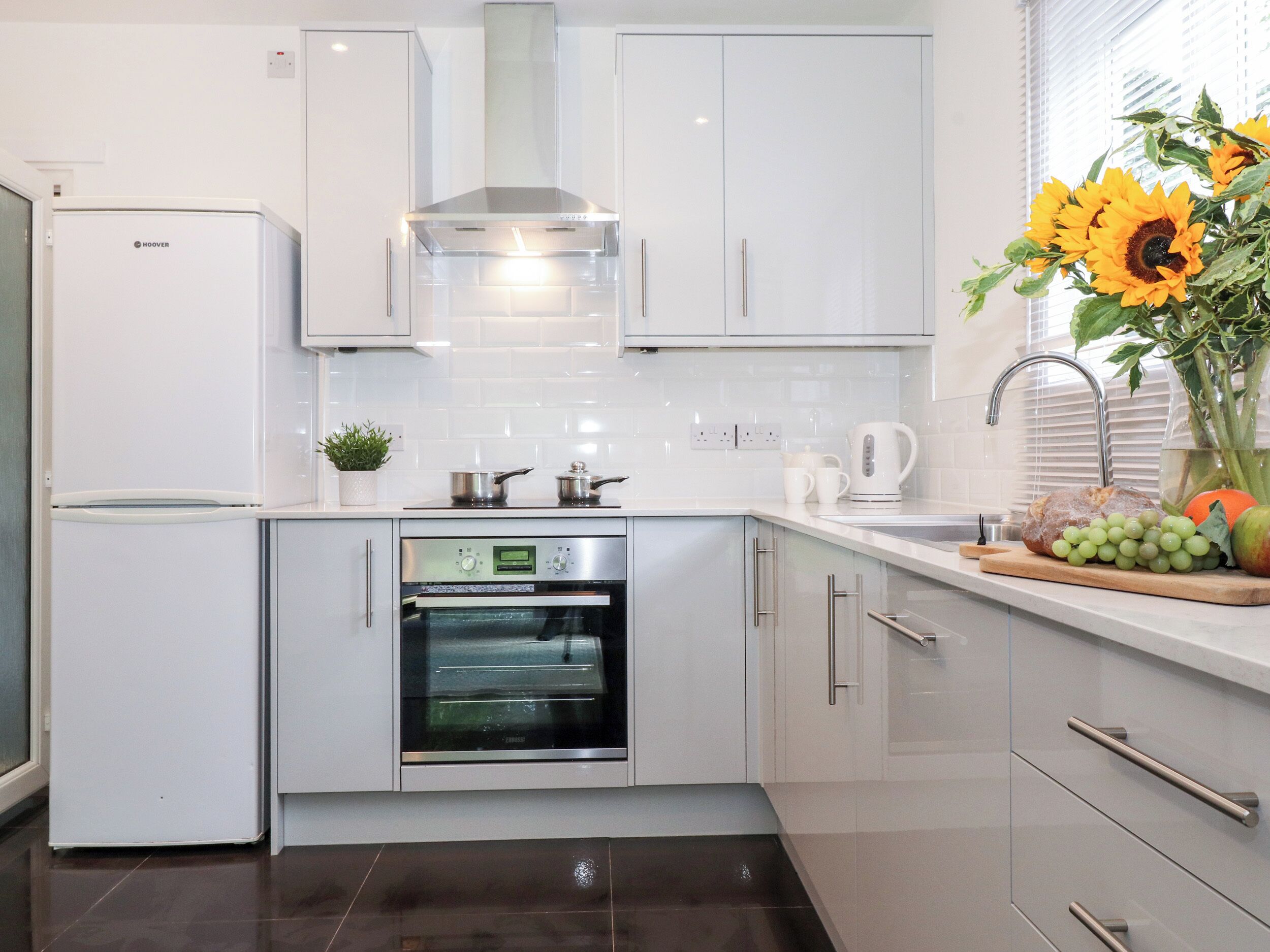 A modern kitchen with white cabinets, a built-in oven, and a stainless steel range hood.
