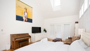 A bedroom with a large bed, a piano, a TV, and a painting on the wall.