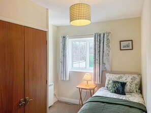 A bedroom with a wooden wardrobe, a window with curtains, a bedside table with a lamp, and a bed with floral bedding. - Escape to this wonderful holiday cottage in Helperby, North Yorkshire. (Helperby, near Thirsk)