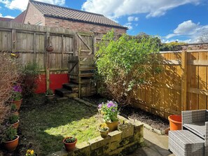 A backyard with a wooden fence, potted plants, a brick wall, and a small set of steps leading to a red door. - Escape to this wonderful holiday cottage in Helperby, North Yorkshire. (Helperby, near Thirsk)