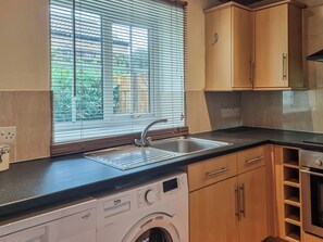 A kitchen with a washing machine, wooden cabinets, a sink, and a window with blinds. - Escape to this wonderful holiday cottage in Helperby, North Yorkshire. (Helperby, near Thirsk)