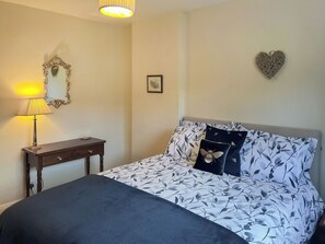 A bedroom with a bed, a bedside table, a lamp, a mirror, and a wall decoration. - Escape to this wonderful holiday cottage in Helperby, North Yorkshire. (Helperby, near Thirsk)