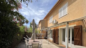A patio with a table and chairs, a covered seating area, and a building with shutters and an air conditioning unit.