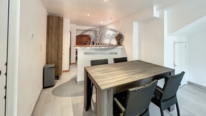 A modern kitchen with white cabinets, a wooden island, and a dining area with a wooden table and wicker chairs.