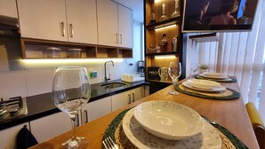 Une cuisine moderne avec un coin repas aménagé pour deux personnes, comprenant une télévision, des verres à vin et une collection d’assiettes soigneusement disposées.