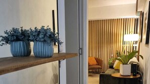 Un intérieur moderne avec un plancher en bois, un canapé, une petite table avec une lampe et deux plantes en pot sur une étagère.