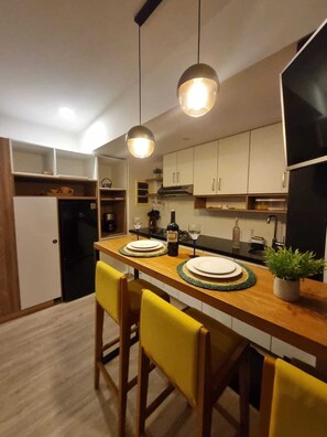 A compact kitchen with a wooden island, two pendant lights, and yellow chairs.