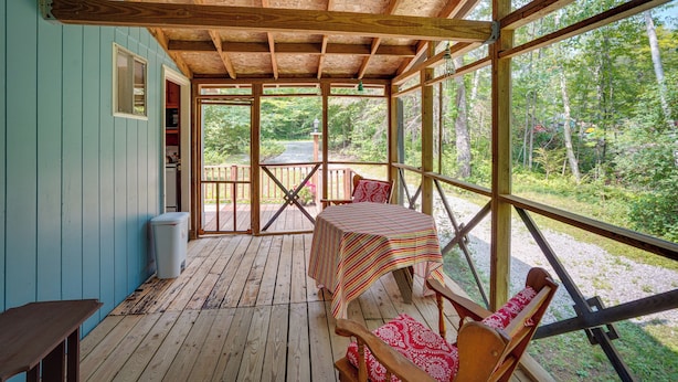 Una terraza de madera con una mesa y sillas, una ventana y vistas al bosque.