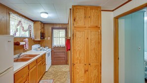 Cocina con gabinetes de madera, un lavamanos y una estufa. Hay una puerta que da a otra habitación.
