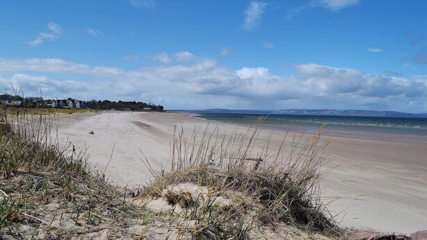 Une plage avec un ciel dégagé, un rivage sablonneux et des bâtiments situés au loin.