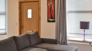 Un salon avec un canapé gris, une petite table, une porte avec une fenêtre et une lampe.